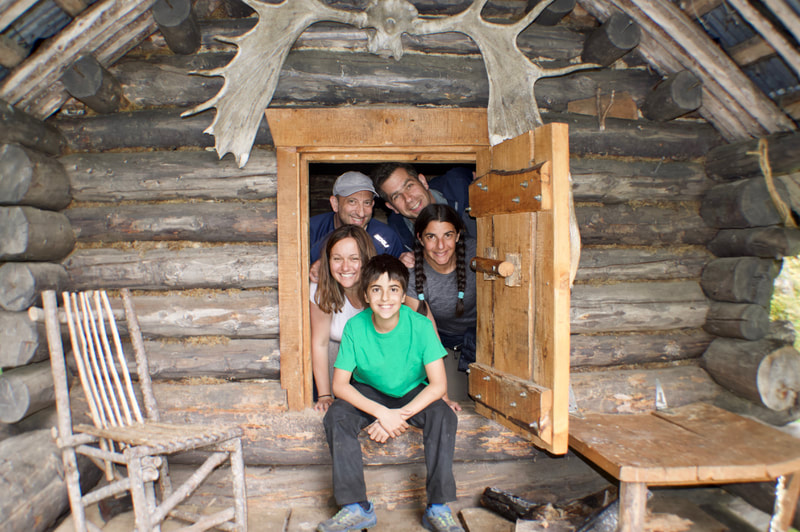 A smiling family posing in a tiny doorway of an old trapper's cabin on their hike to Moose Valley. 