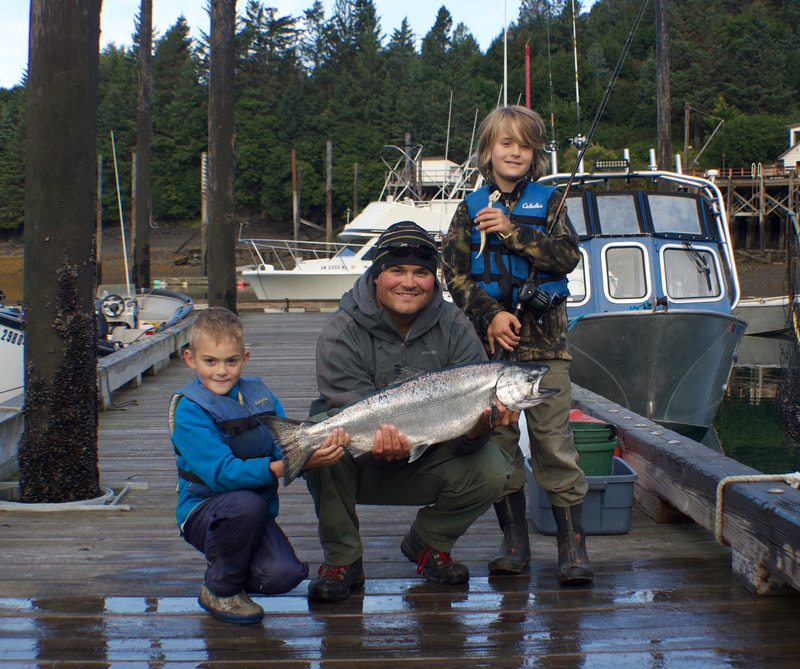 A man and his two young sons holding a salmon at the Halibut Cove dock. 