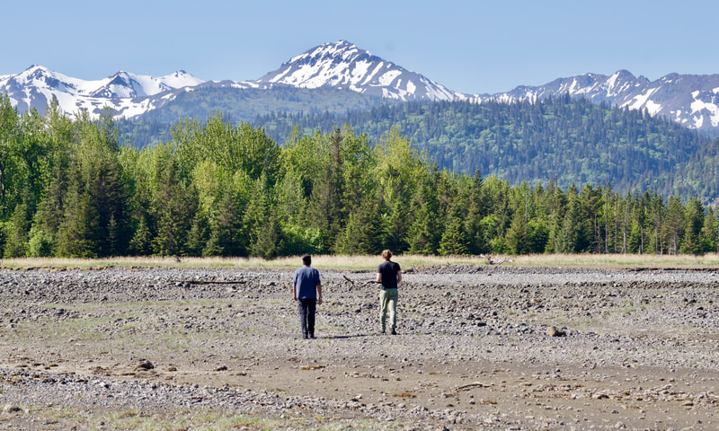 Two men beachcombing on Glacier Spit with snow-capped mountains in the background. 