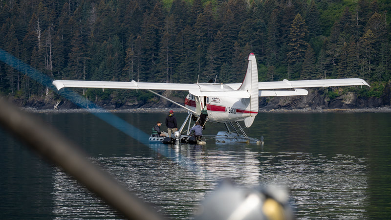 Guests climbing from a small rubber boat into a float plane on the water. 