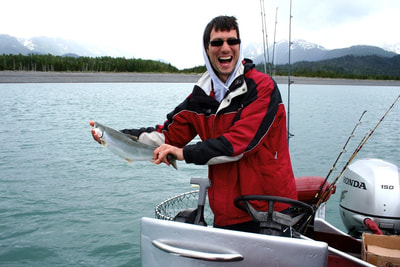A gentleman laughing while holding a small jack salmon he caught trolling.