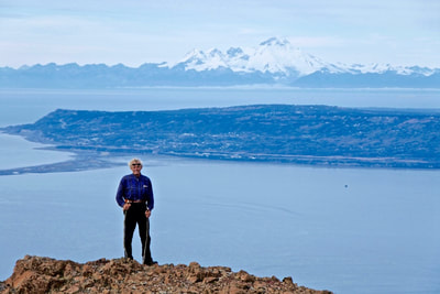 A hiker posing on top of Alpine Ridge with the Homer Spit in the background. 